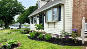 A residential house with a well-maintained lawn, a small garden with various plants, and a white picket fence. - 24 Riverbank Road. Footbridge Beach Cape! (Ogunquit)