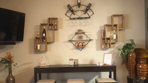 A bar area with stools, shelves with bottles, and a television. - TinkerBell’s Smart Townhome  3BR & 3BA w/ a heated Pool 10 miles from Disney (Clermont)