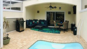 A covered patio with a pool, outdoor seating, and a ceiling fan. - TinkerBell’s Smart Townhome  3BR & 3BA w/ a heated Pool 10 miles from Disney (Clermont)