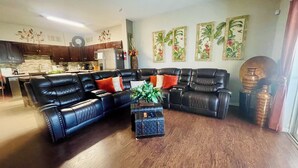 A living room with a sectional sofa, a small side table with a plant, and a kitchen in the background. - TinkerBell’s Smart Townhome  3BR & 3BA w/ a heated Pool 10 miles from Disney (Clermont)