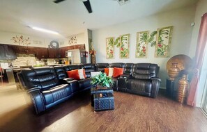 A living room with a sectional sofa, a small side table with a plant, and a kitchen in the background. - TinkerBell’s Smart Townhome  3BR & 3BA w/ a heated Pool 10 miles from Disney (Clermont)
