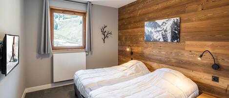 Un dormitorio con cama, ventana con cortinas, un cuadro colgado en la pared, mesita de noche y lámpara de pared.