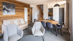 Ett modernt vardagsrum med en väggpanel i trä, en matplats med ett träbord och stolar, en soffa och en trappa som leder upp till en övre våning.