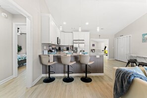 A modern kitchen with a central island, bar stools, and a dining area with a table and chairs.