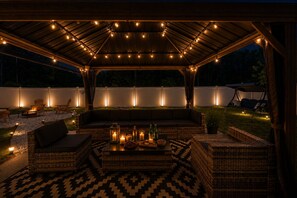 An outdoor patio with wicker furniture, a fire pit, and string lights.