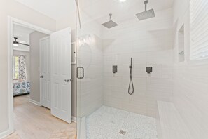 Un bagno moderno con doccia a pavimento, pareti rivestite di piastrelle bianche e una porta che dà su un'altra stanza.