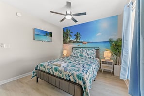 A bedroom with a bed, a ceiling fan, a wall mural, a nightstand, and a potted plant.