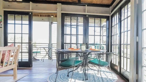 Un patio techado al aire libre con una mesa redonda y sillas, ventanas amplias y techo de madera.