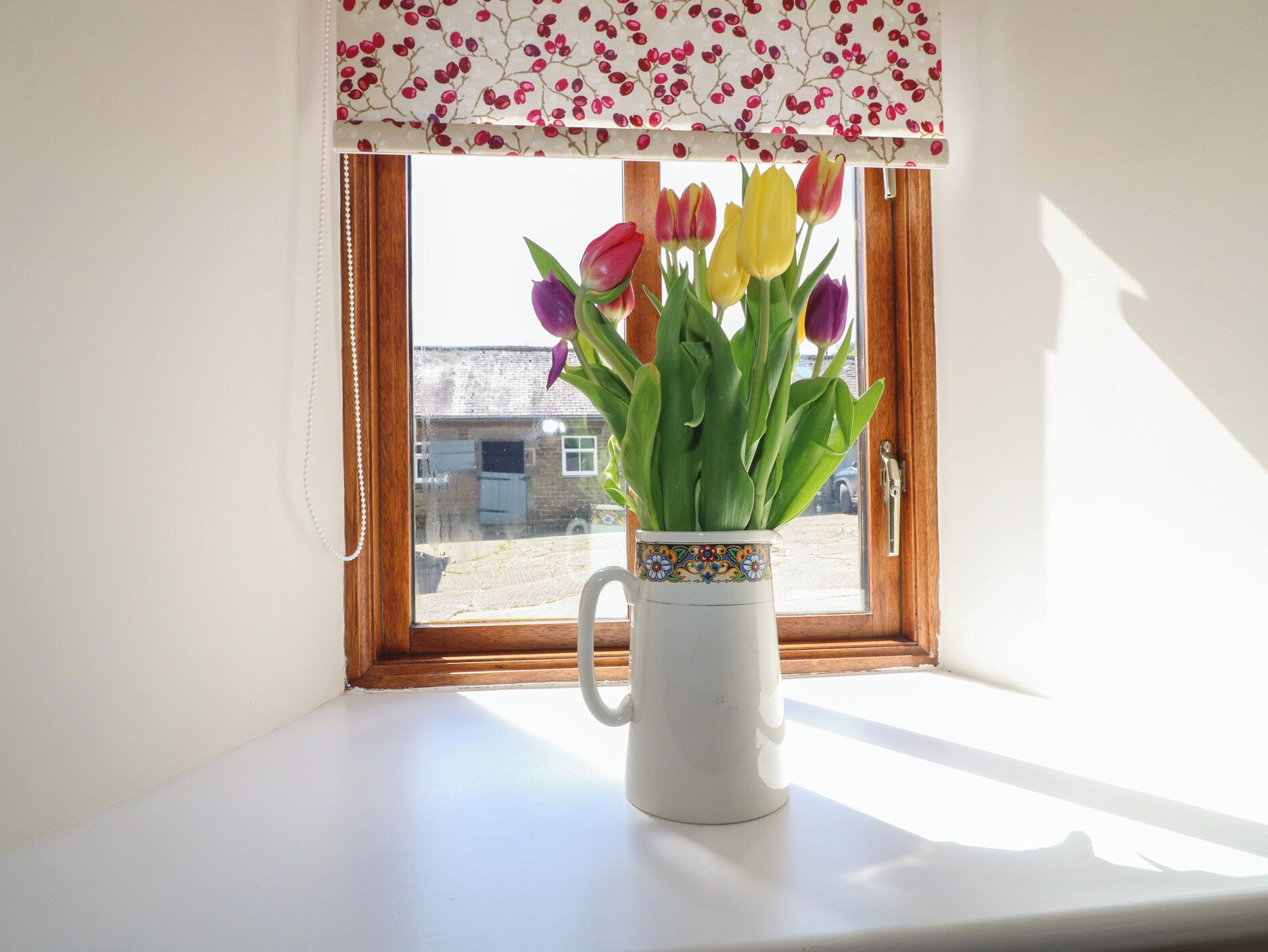 A window with a white vase containing tulips, a wooden window frame, and a white wall.