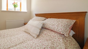 A bedroom with a wooden headboard, floral bedding, a radiator, and a window with a view of flowers.