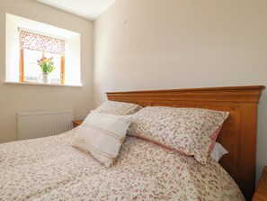 Un dormitorio con cabecera de madera, ropa de cama floral, un radiador y una ventana con vistas a flores.