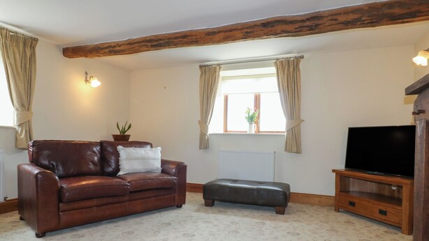 A living room with a leather sofa, a wooden TV stand, and a window with curtains.