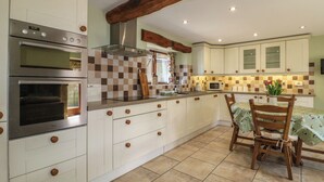 A kitchen with white cabinets, a wooden beam ceiling, a microwave, and a wooden dining table.