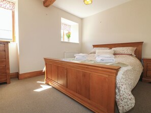 Ein Schlafzimmer mit einem hölzernen Bett, einem Fenster mit Blick auf Blumen, einem Heizkörper und einer hölzernen Kommode.