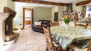 A cozy living area with a fireplace, a dining table with a floral tablecloth, and a kitchen in the background.