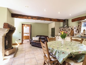 A cozy living area with a fireplace, a dining table with a floral tablecloth, and a kitchen in the background. - Carr House Farm (Chesterfield)