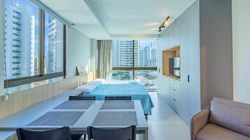 Quarto de hotel moderno com uma janela grande, uma cama, uma mesa de jantar e um sofá.