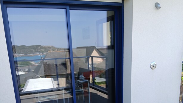 A modern building with a glass sliding door leading to an outdoor deck. - STUDIO sea and cape view 2pers. (Erquy)
