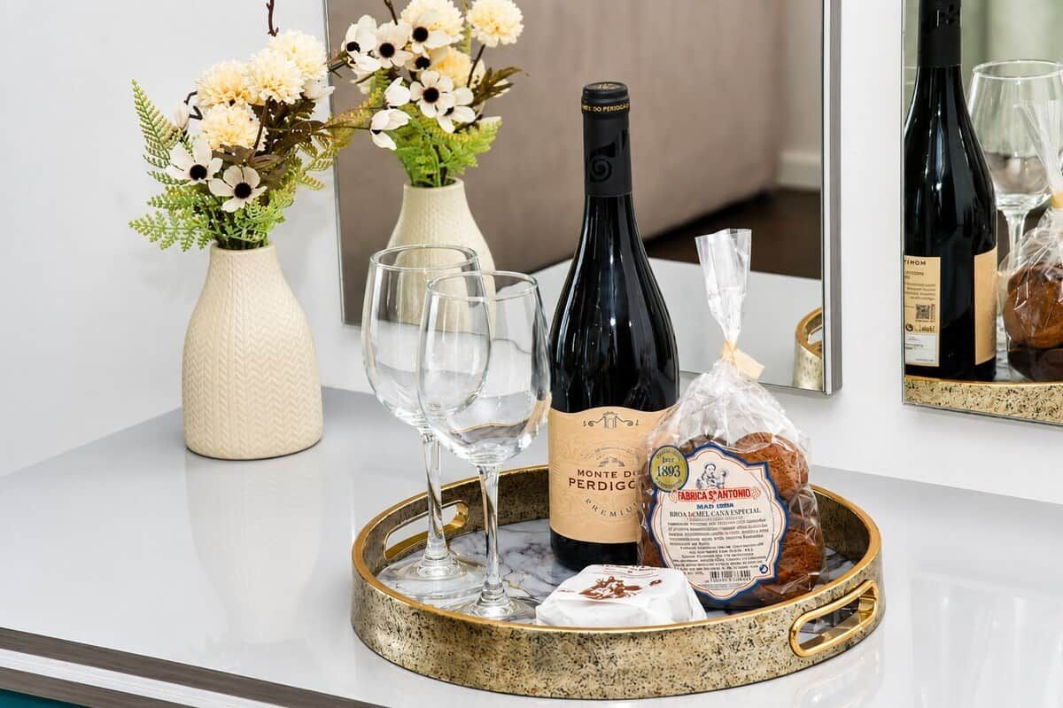Een tafel met een fles wijn, glazen, een vaas met bloemen en een schaal met brood en kaas.
