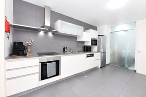 A modern kitchen with white cabinetry, a built-in oven, a stainless steel refrigerator, and a microwave.