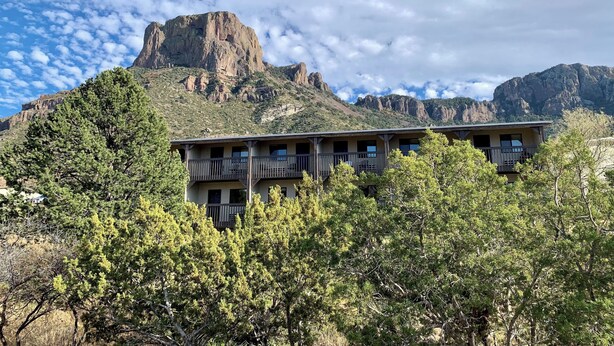 A building with multiple balconies, surrounded by trees and mountains in the background.