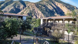 A building with a staircase leading to a balcony, surrounded by trees and a mountain in the background.