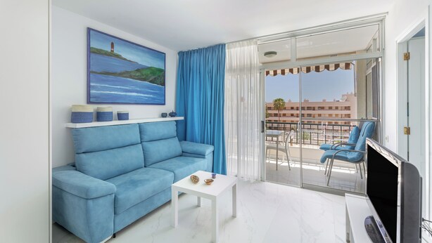 Un salon moderne avec un canapé bleu, une table basse blanche et un tableau représentant un phare.