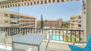 Un balcon avec une table et des chaises, donnant sur une piscine et des immeubles.
