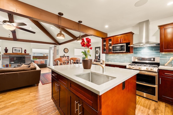 A modern kitchen with a large island, wooden cabinets, stainless steel appliances, and a ceiling fan.