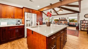 A modern kitchen with wooden cabinets, a large island, and a dining area with a sofa and bookshelves. - 25% Off Sept WkDay Great 4 Families, Walk 2 Beach! (Ventura)