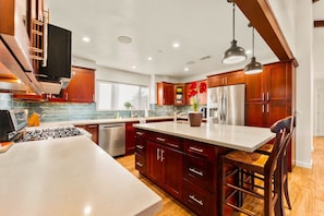 A modern kitchen with wooden cabinets, a central island, stainless steel appliances, and pendant lighting.