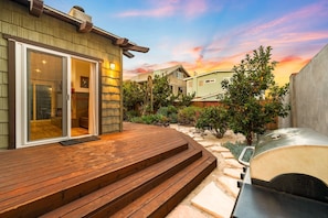 A patio with wooden steps, a barbecue grill, and a house with a sliding glass door.