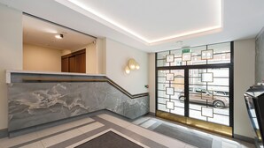 En hotellobby med en marmordiskinredning i receptionen, en trappa och utsikt över gatan genom en glasdörr.