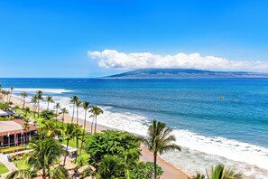 A beach view with palm trees, a clear sky, and a distant mountain. - Ocean Front steps from beach, dining, shopping 1051 (Lahaina)