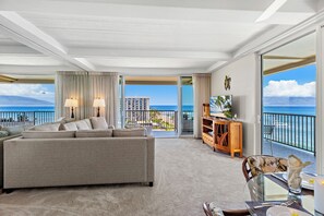 A spacious living room with a large sofa, a dining area with a table, and a balcony with a view of the ocean. - Ocean Front steps from beach, dining, shopping 1051 (Lahaina)