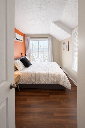 A bedroom with a bed, a window with curtains, a ceiling fan, and a door. - Lake Breeze Stylish Beach Boho 1BD w/ Private Deck (Michigan City)