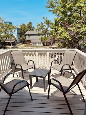 A deck with four chairs and a table, surrounded by a wooden railing, overlooking a residential area with houses and trees. - Lake Breeze Stylish Beach Boho 1BD w/ Private Deck (Michigan City)