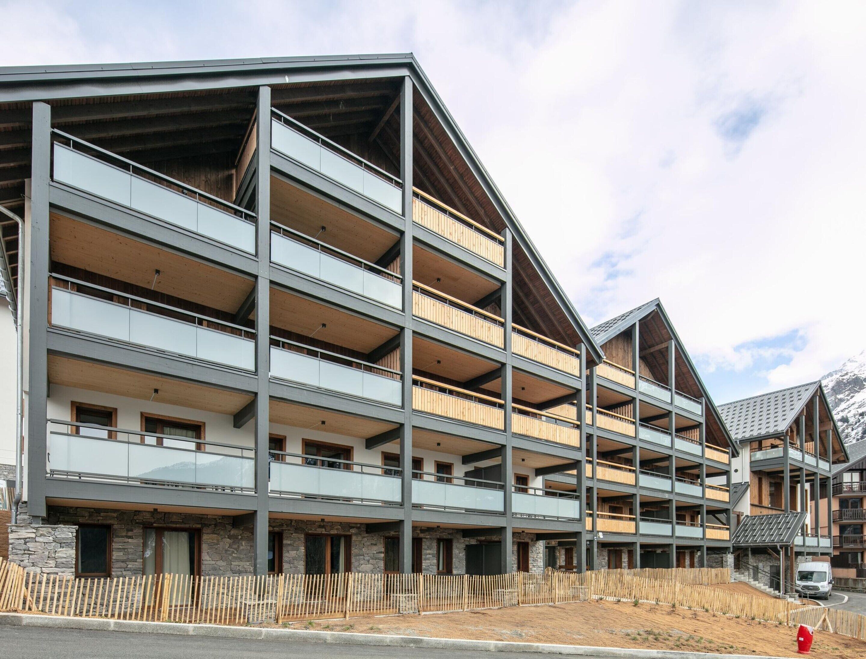 A multi-story building with balconies, stone facade, and a ski slope in the background.