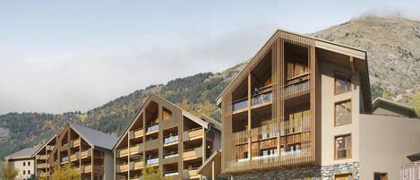 Un hôtel moderne à plusieurs étages, doté de balcons, d’un mur en pierre et offrant une vue sur un paysage montagneux.