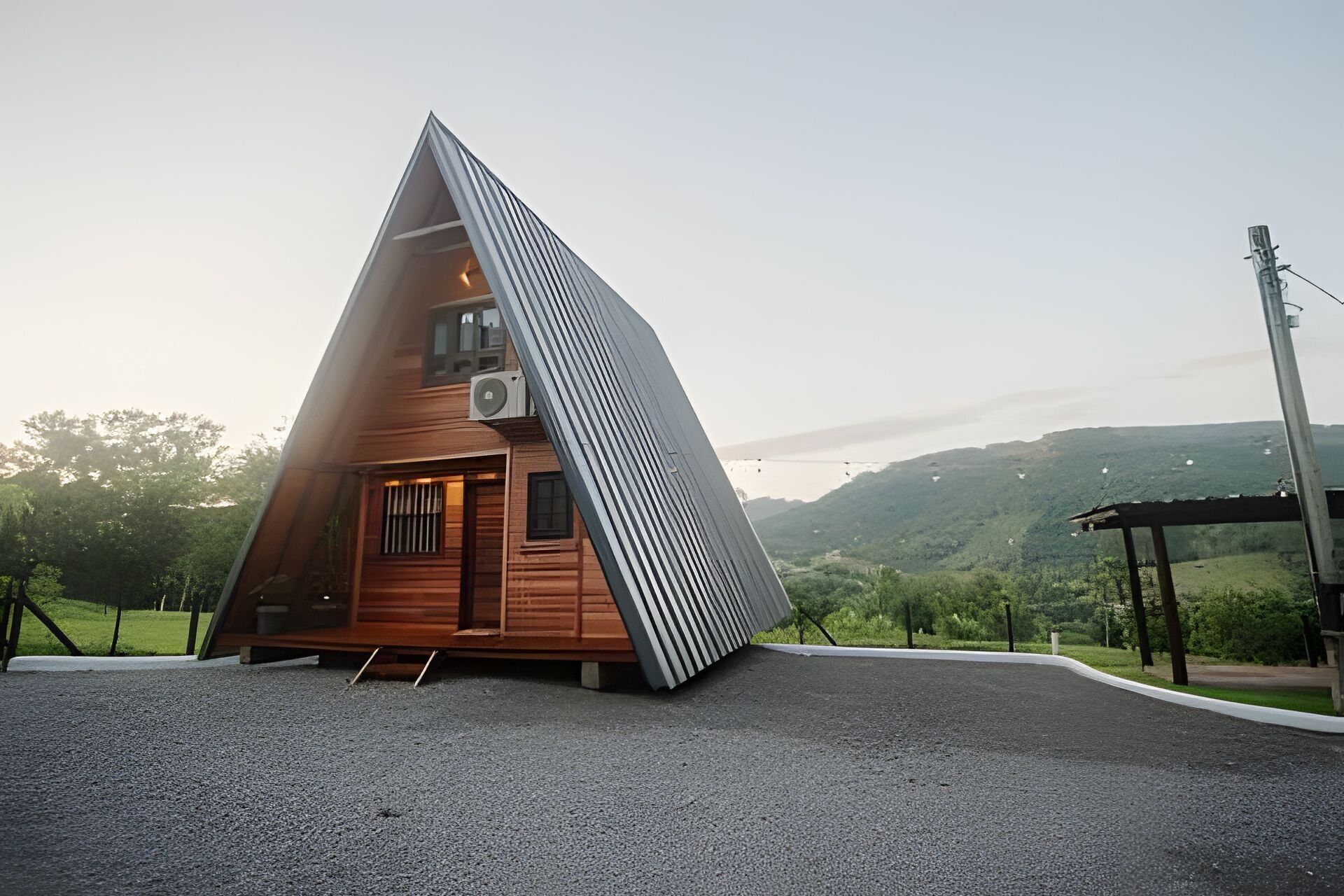 Una cabaña de madera triangular con techo inclinado, un pequeño porche y un equipo de aire acondicionado.