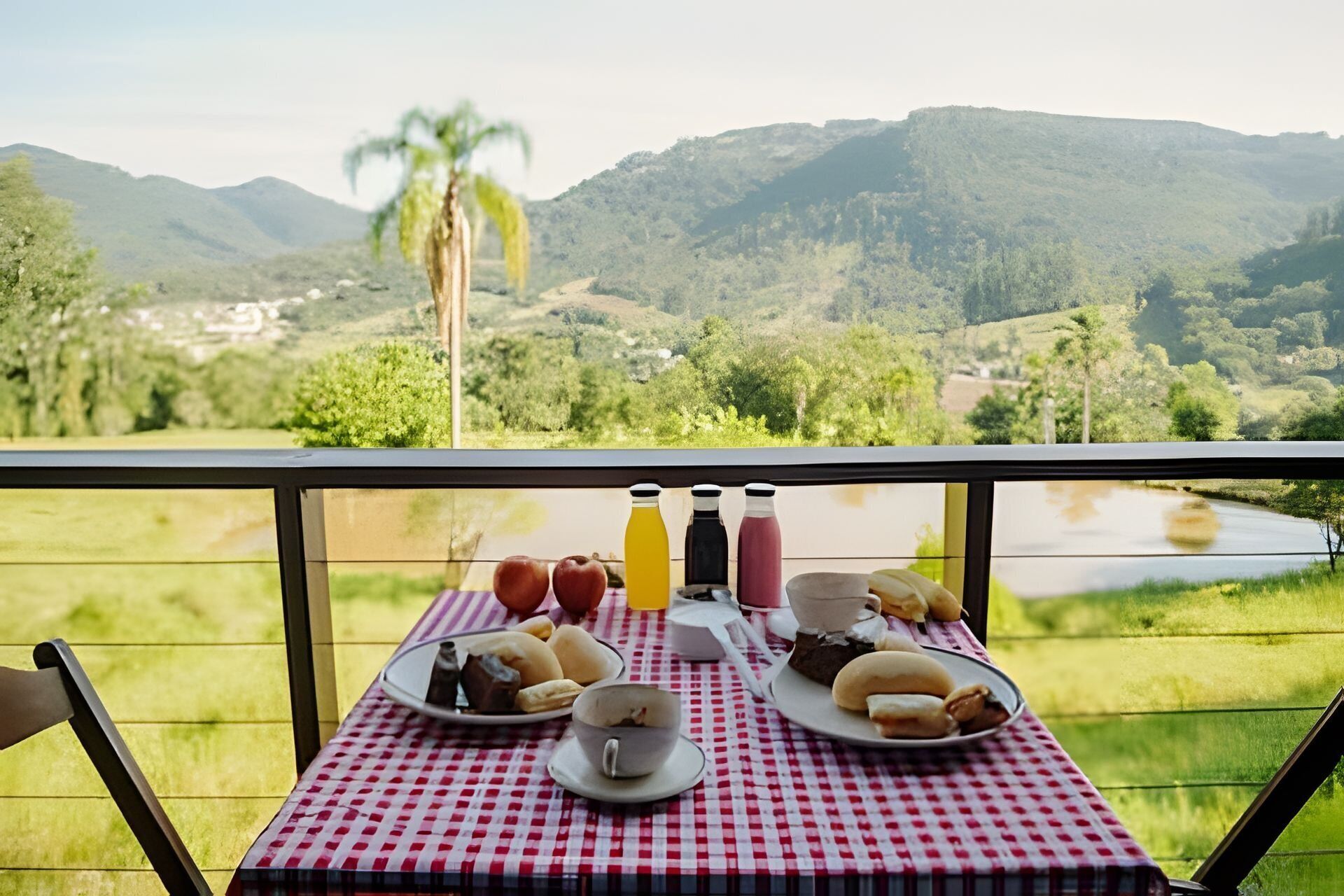 A table with breakfast items and bottles, overlooking a scenic landscape with hills and a body of water.