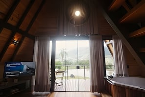 A room with a television, a wooden ceiling, a sliding glass door to a balcony, and a bathtub.
