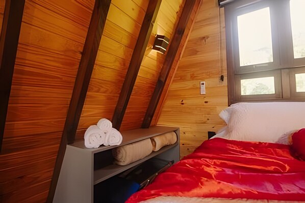 Une chambre dans un chalet en bois, avec un lit, une étagère avec des serviettes et une fenêtre.