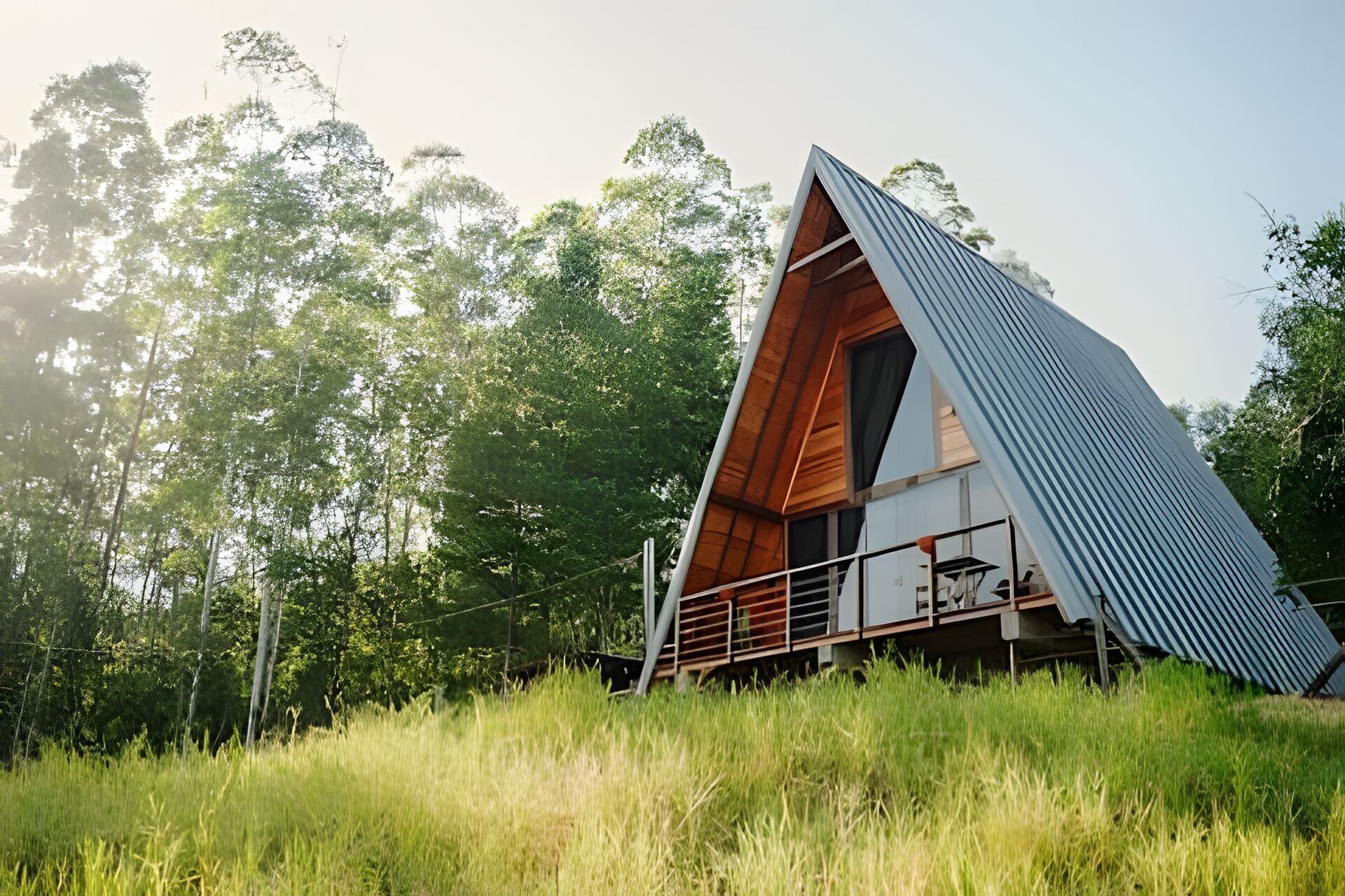 Une cabane moderne en bois, de forme triangulaire et dotée d’un toit incliné, entourée d’une végétation luxuriante.