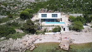 Uma villa moderna com piscina, rodeada por terreno rochoso e vegetação.
