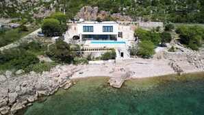 Uma villa moderna com piscina, rodeada por terreno rochoso e vegetação.