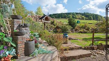 A garden with a stone wall, a wooden birdhouse, and a metal pot.