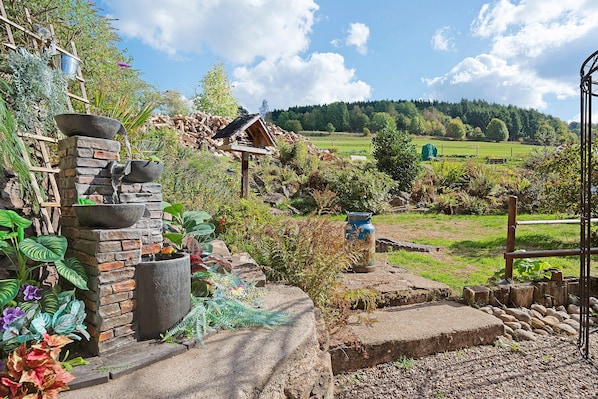 A garden with a stone wall, a wooden birdhouse, and a metal pot. - Guesthouse 'Chambre Chevaucheurs' with Shared Terrace & Garden, Wi-Fi (Gerbépal)