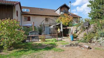 Une maison de campagne avec un toit en tuiles, une clôture en bois et un jardin agrémenté d’un portail en métal.