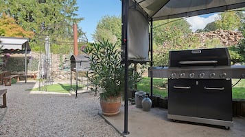 An outdoor patio with a barbecue grill, a pergola with a canopy, and a potted plant.